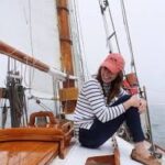 Woman sailor on a boat. A wooden sailboat. She is smiling and wear a red hat