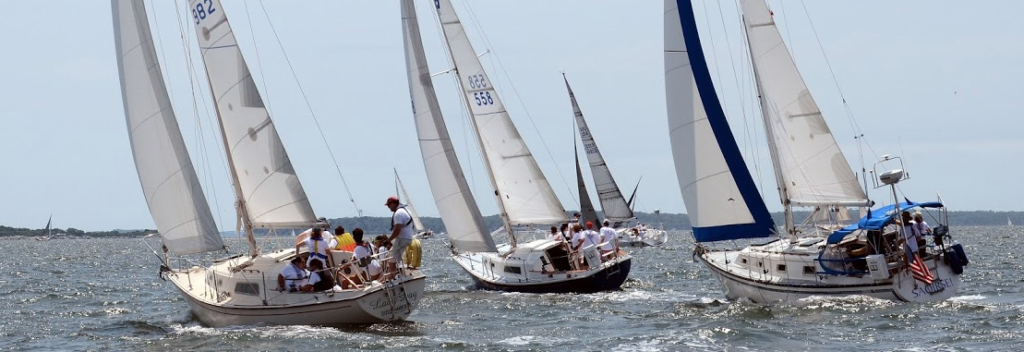 3 sailboats at the start of an annual regatta. many crew members on board. 