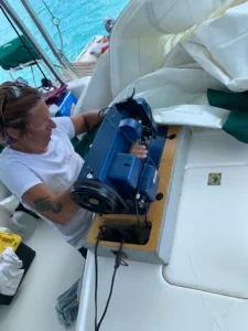 Kim sewing the headsail to repair the sail damage with a big sewing machine on board of a catamaran.