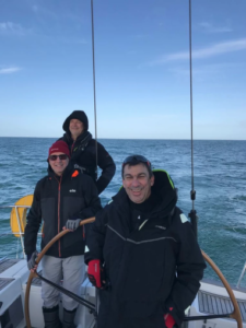 Three smiling sailors on a sailboat.