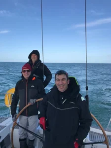 three men sailing. One is at the helm. They all smile.