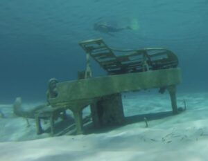 Underwater piano resting on white sand